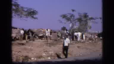 India (1970): A Man Walks On A Road Beside A Community Of People On The Outskirts