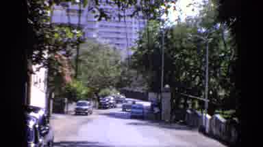 India (1970): Blue Car Driving Away From White Building On A Sunny Day