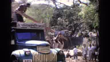 India (1970): People Loading Lumber Into Green Truck On A Bright Sunny Day
