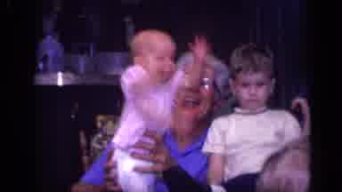 California USA (1968): Baby Girl Jumping Inside Grandmother's Hands While A Boy Is