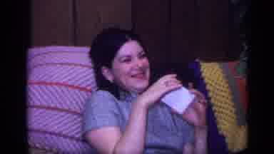 California USA (1968): Woman Wearing Black Shirt Sits On Brown Sofa Holding Baby