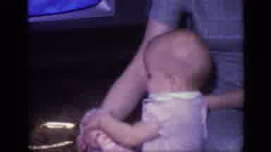 California USA (1968): Small Baby With Pink Dress Playing With A Doll While A