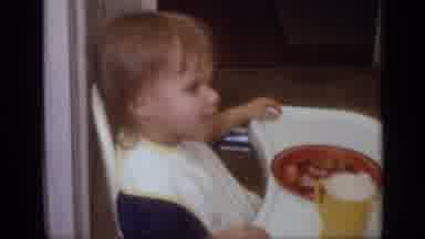 California USA (1968): Baby Wearing White Bib Sits In Highchair With Bowl Of Food