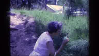 Florida USA (1968): Woman Stops Along Dirt Path And Takes A Big Sniff From A Plant