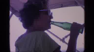 Florida USA (1968): Woman Wearing Sunglasses On Boat Drinks From Green Glass Soda