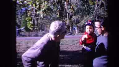 Florida USA (1968): Two Men Holding Baby That Pokes One Man On The Nose In A Park