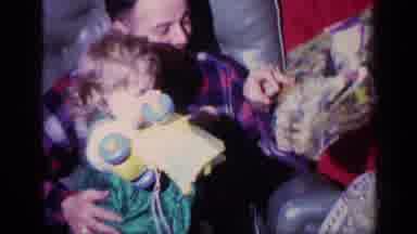 California USA (1969): Father Sitting In An Armchair Holds Daughter Receiving A