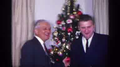 California USA (1969): Two Men Wave As They Stand Beside Holiday Tree One Touches