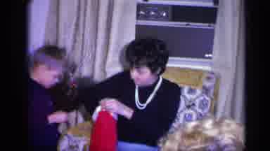 California USA (1969): A Mom Is Unwrapping A Gift While Her Son Daughter And