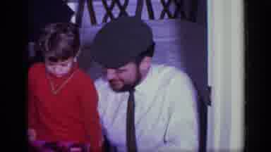 California USA (1969): Child Struggles To Remove Wrapping From Package As He Sits