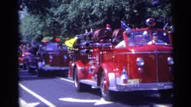 California USA (1969): Procession Of Red Fire Trucks Traveling Down Street On A