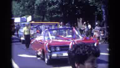California USA (1969): Red Vehicle Moves Down Street Followed By Man In Yellow