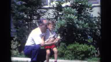 California USA (1969): Man Wearing Blue Pants Holds Hand On Boy Wearing Red Shorts
