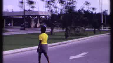 Bahamas (1969): Woman Wearing Yellow Shirt Crossing The Street And Flowers Near