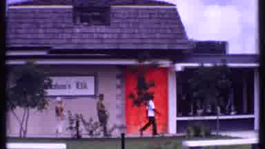 Bahamas (1969): Man In Uniform Leads Man And Lady Then Woman Takes Photographs And