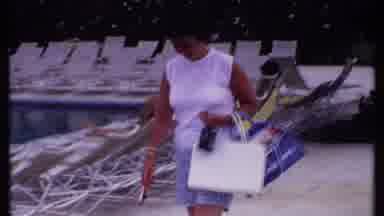 Bahamas (1969): Woman Walking With Bags By Pool Along Chairs Trees And Ocean