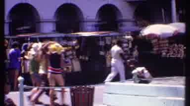 Bahamas (1969): People Walk Around In Large City With Colorful Shops And Cars And