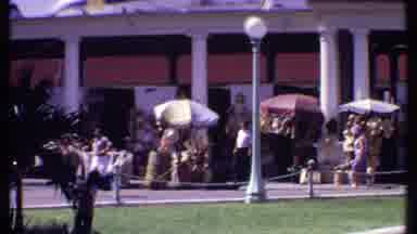 Bahamas (1969): People Walk Around Outside As Others Stay Under Umbrellas As Kid