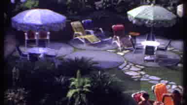 India (1969): Couple Sitting On Orange Lounge Chairs By Pool On A Sunny Day