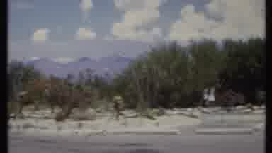 California USA (1971): People Walking Around The Bush On A Desert With A Building
