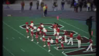 Ithaca New York (1979): Girl Cheerleaders Wave Pom Poms In Front Of Boy