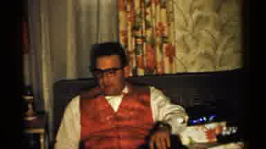 New Hampshire (1952): Man Wearing Red Suit And Glasses Sits On Gray Sofa Talking