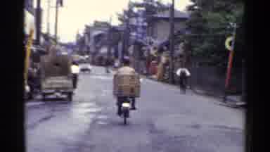 Japan (1953): Biker With A Large Basket Behind Him Pedals On A Busy Street