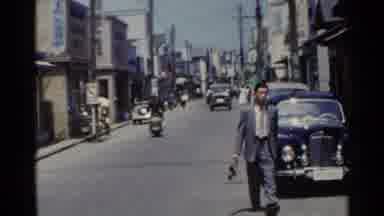 Japan (1953): Residents Bike And Walk To Work On A Bustling Town Street