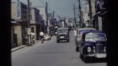 Japan (1953): Gray Jeep And Blue Car Driving Down Street On A Bright Sunny Day