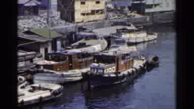 Japan (1953): Small Boats Docked At A Port With Buildings In The Background And