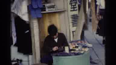 Japan (1953): An Asian Man Shining Or Fixing Shoes On A Busy Day While A Customer