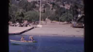 California (1955): Man Wearing Blue Shirt Waves At Camera While Standing In Boat
