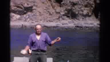 California (1955): Man Wearing Blue Shirt Standing In Boat Holding Small Object On