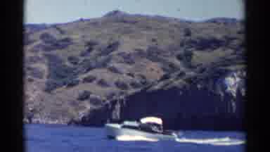 California (1955): Power Boat With Canopy Sails Through Water Near Steep Hills