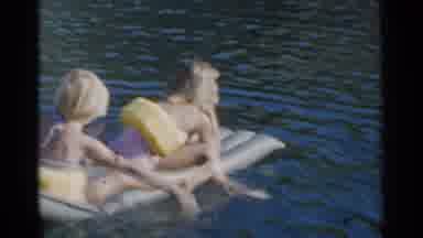 California (1955): Two Kids Sitting On Grey Inflatable Pool Raft On A Sunny Day