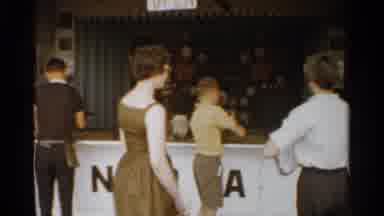 San Francisco (1959): Woman Wearing Brown Dress Walks Past Game Booth On A Clear