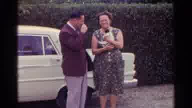 Germany (1961): Man Dressed In Suit Standing Next To Woman In A Dress Holding A