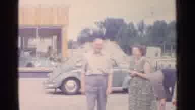 Germany (1961): Two Old People Standing In Front Of An Old Car Smiling At The