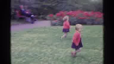 SWITZERLAND-1961: Twin Girls Wearing Red Sweaters Run Through Grass On A Clear