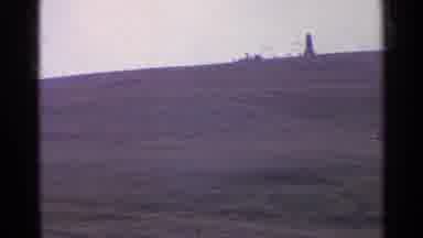 Switzerland (1961): A Field With Short Grass And Hills And A Tower In The