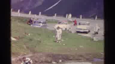 Switzerland (1961): Woman In White Coat Runs Up Grassy Hill Near Parking Lot While