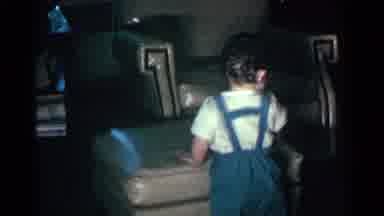 Kentucky USA (1963): Toddler Wearing Blue Overalls Throws Newspaper From Tan A