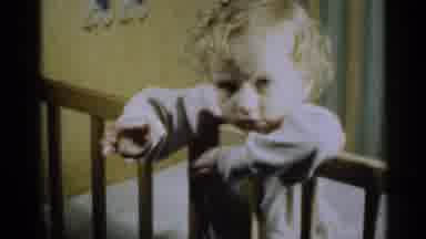 Michigan USA (1939): Baby Wearing White Pajamas Stands In Yellow Crib Folding