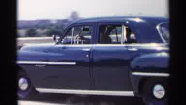 New York USA (1954): Vintage Black Sedan Drives Down City Road Driver Has Hand Out