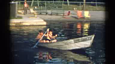 New York USA (1954): Two Boys Row A Canoe In A Lake; Behind Them On The Shore Are