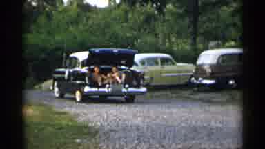 New York USA (1954): People Sitting On The Back Of A Car Trunk As It Drives Down