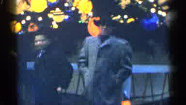 New York City (1955): Man Wearing Grey Coat Stands Next Multicolored Outdoor Light