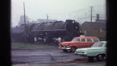 Duluth Minnesota (1960): Red Car Drives Past Black Locomotive In A Cloudy Day