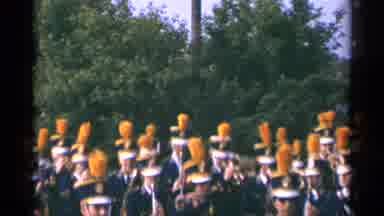 Minnesota USA (1964): Marching Band Marching Down Road As People With Flags Follow