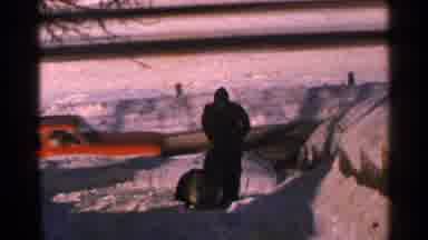 Minnesota USA (1965): Man Wearing Black Coat Pushes Snowblower As Red Car Drives